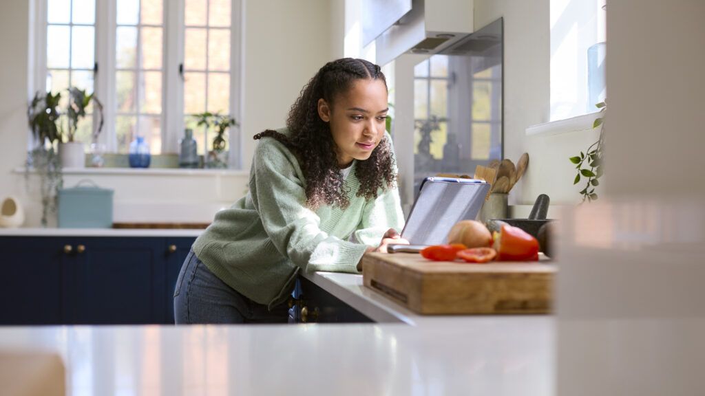 Teenage girl looking up the ingredients to a content cookbook in the kitchen